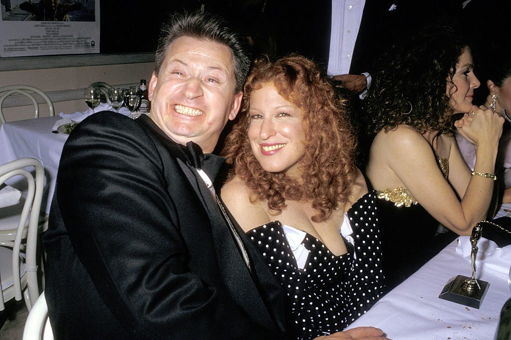Matthew von Haselberg and Bette Midler smiling while sitting at a table at the Swifty Lazar Oscar Party in1988