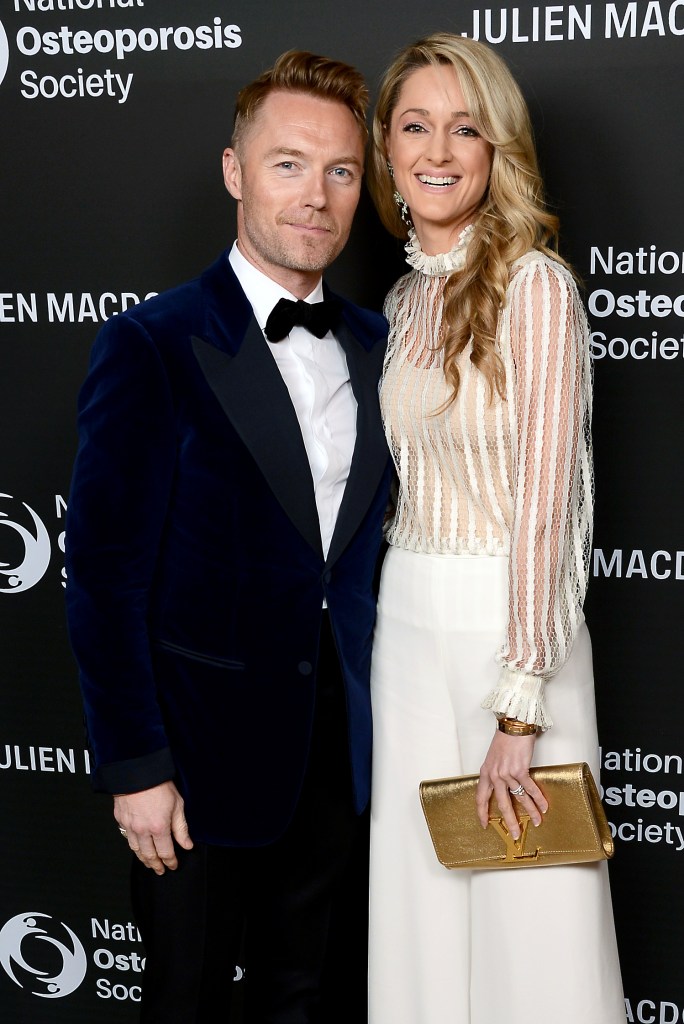 Ronan Keating in a blue velvet suit and Storm Keating ina white lace top and matching trousers posing with their arms around each other at an event