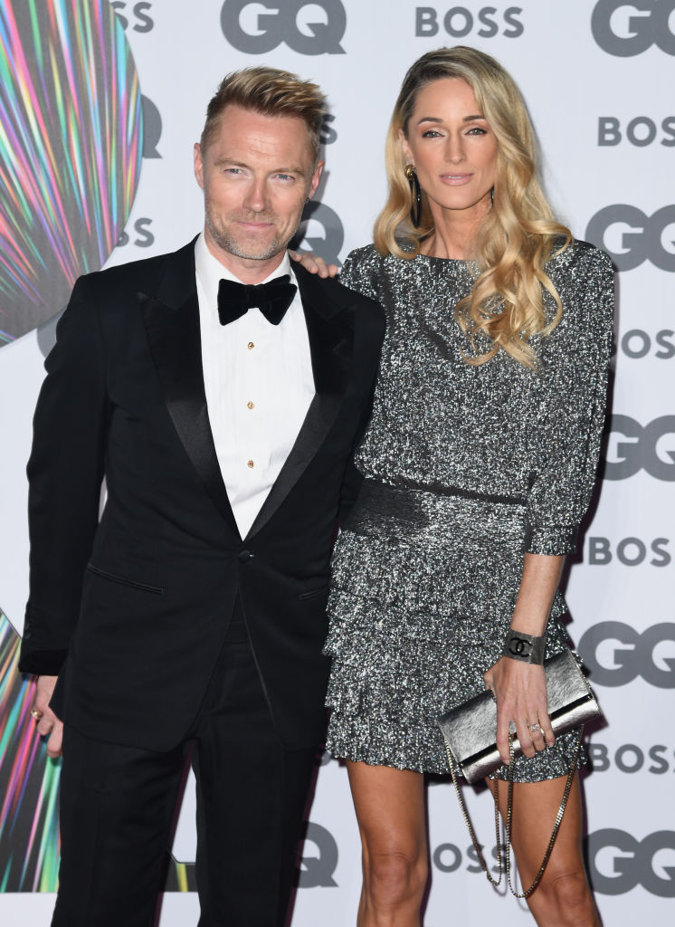 Ronan Keating in a black tuxedo and Storm Keating in a silver dress posing with her arm on Ronan's shoulder at an event