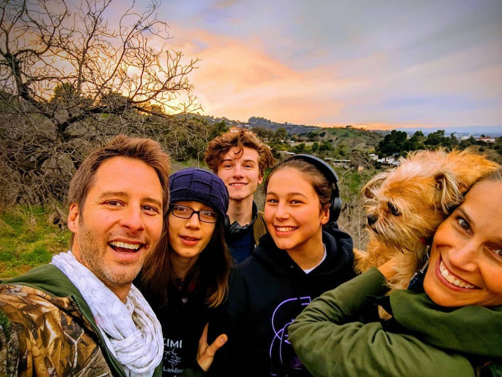 Chesney Hawke and wife pose with their children in the outdoors, with an orange and purple sky behind them