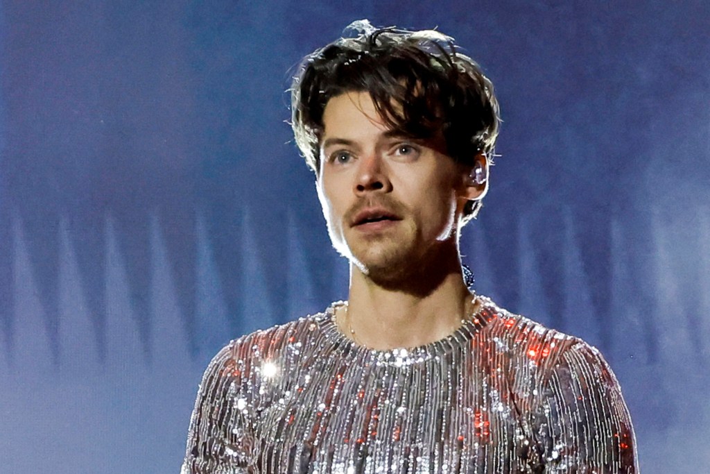 Harry Styles with shorter, curly hair and wearing a sparkling silver top during a performance at the Grammys 