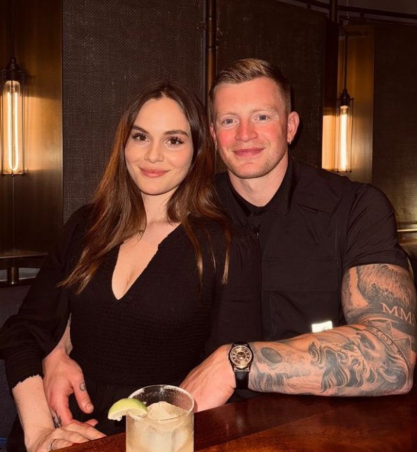 Adam Peaty wearing a black shirt with his arm around girlfriend Holly Ramsay wearing a black top