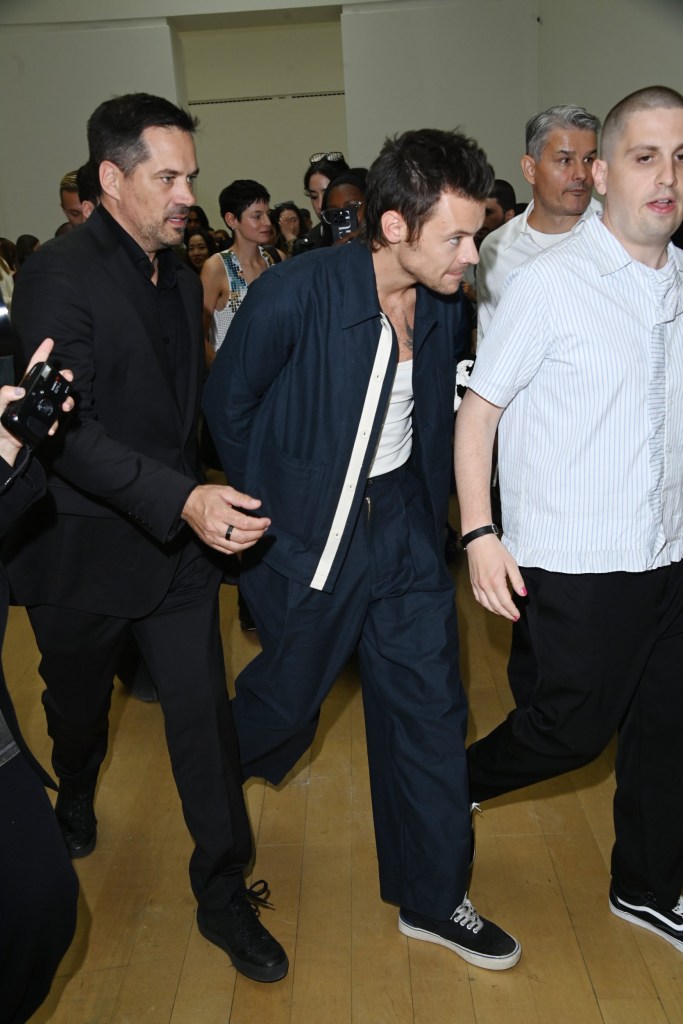 Harry Styles showcasing his new hairstyle and wearing a navy outfit with trainers, leaving a London Fashion Week show