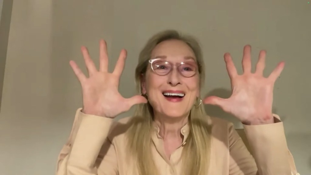 Meryl Streep with her hands in the air smiling on video call 