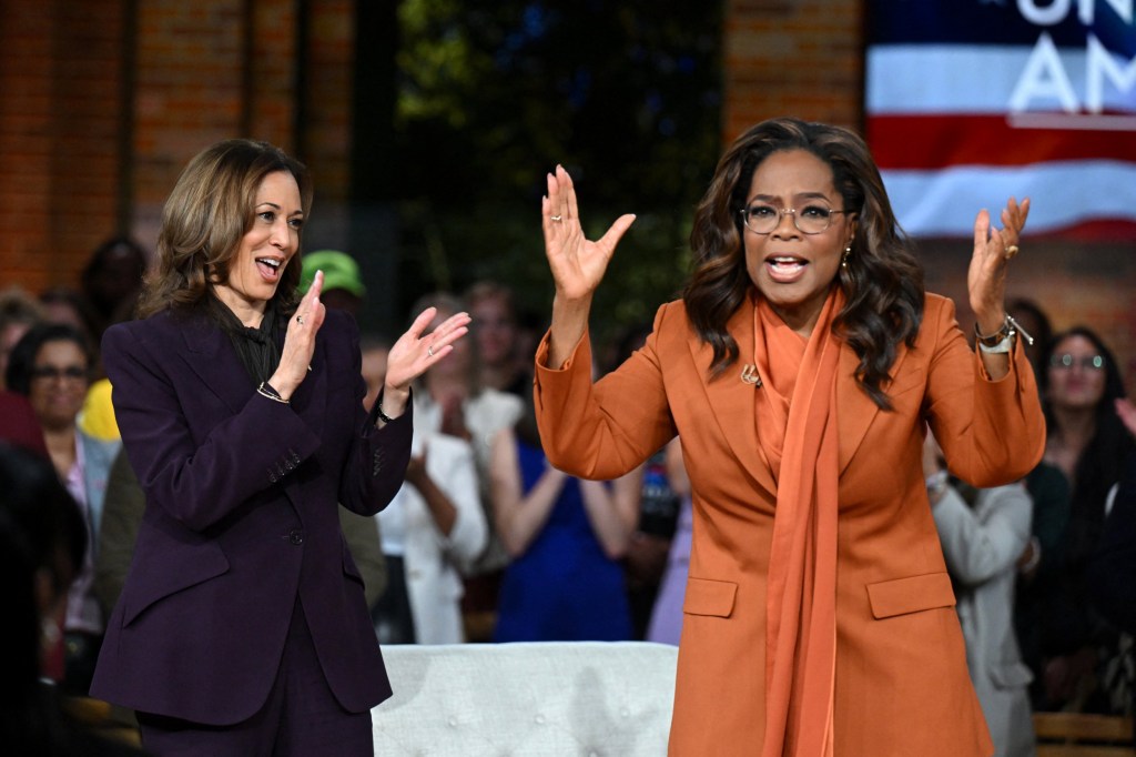 Kamala Harris clapping alongside Oprah Winfrey, who is gesturing with her hands