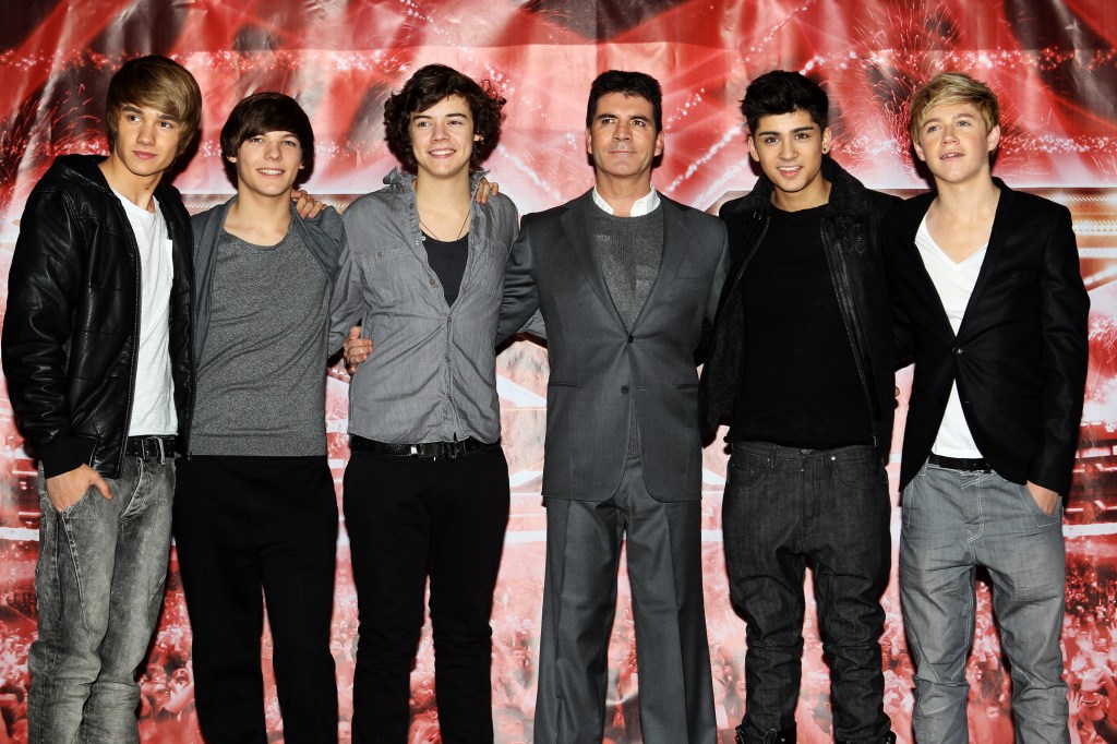 One Direction and Simon Cowell stand with their arms around each other at an event for The X Factor