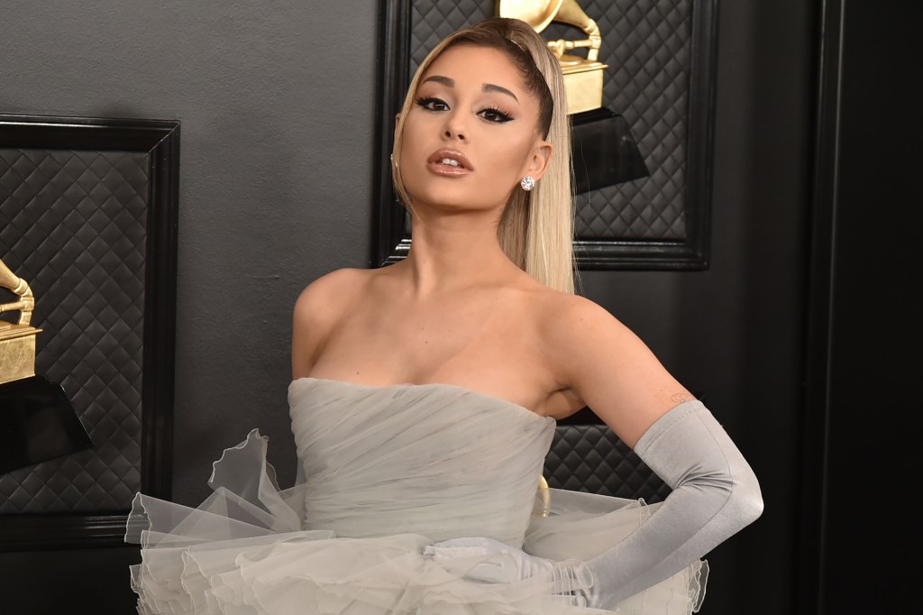 Ariana Grande poses for a photo at a carpet event, wearing a grey strapless gown and long gloves