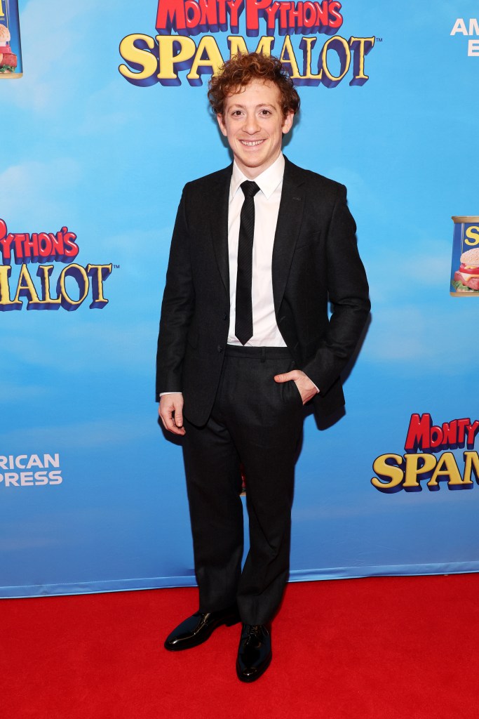 Ethan Slater poses for a photo on red carpet in a black suit with white shirt