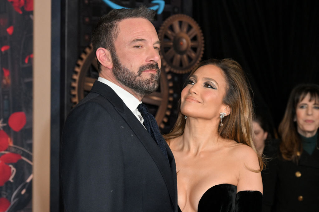 Jennifer Lopez looks up towards Ben Affleck and smiles, as they stand together on a red carpet