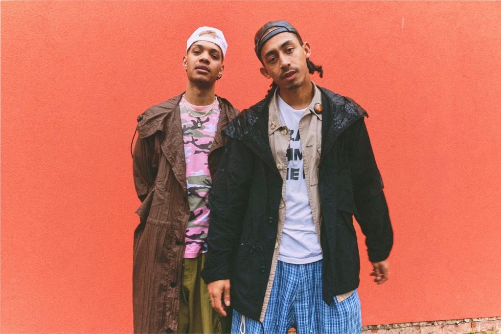 Rizzle Kicks pose against orange wall.