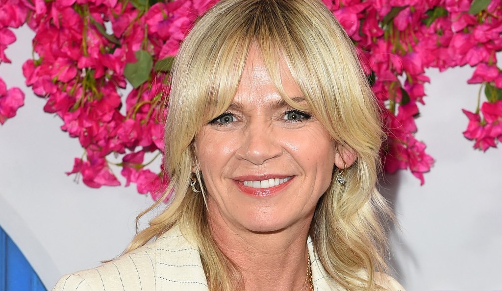 Zoe Ball smiles for a photo aganst pink flowers