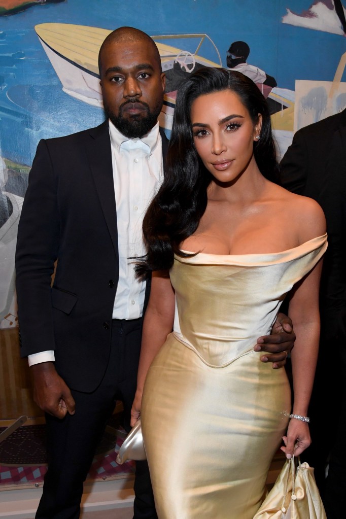 Kanye West and Kim Kardashian West pose at an event in 2019. He wears a black suit and she wears a gold, strapless dress