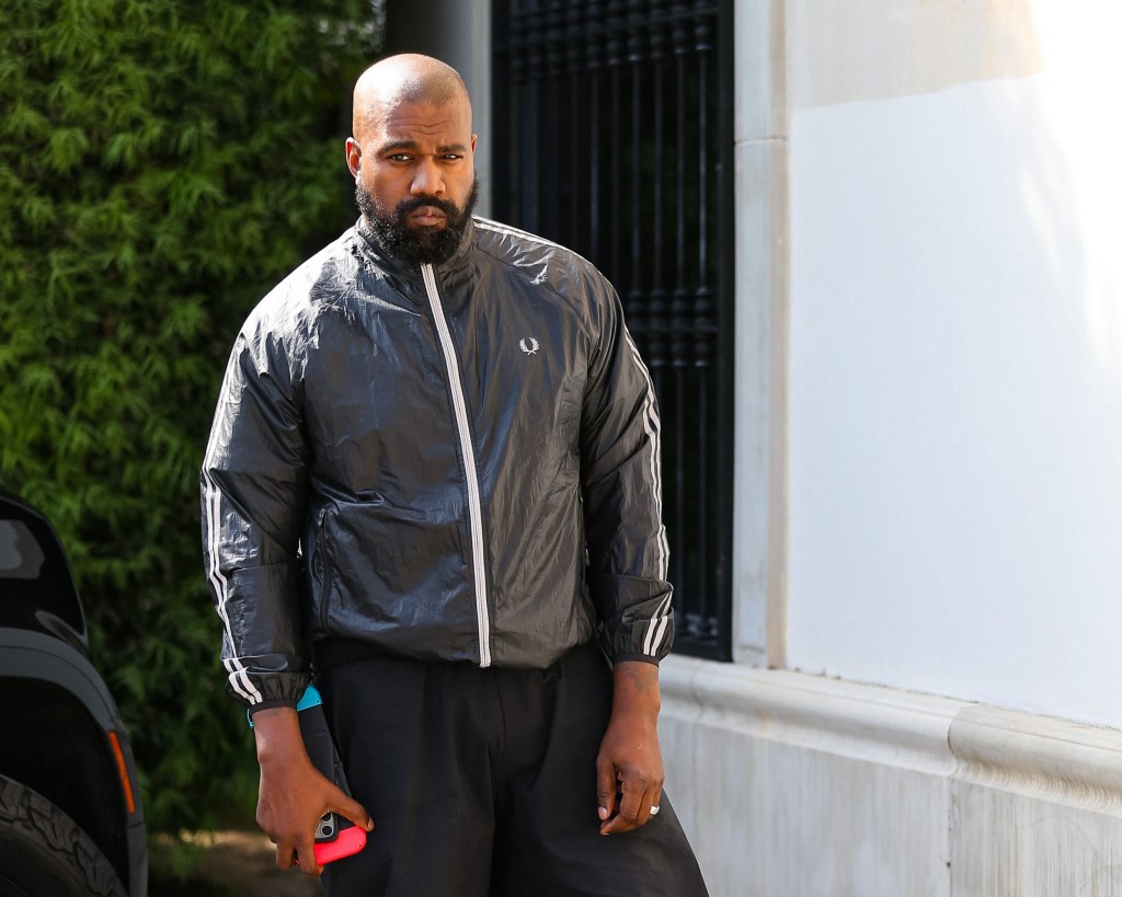 Kanye West standing on a street in Los Angeles earlier this year, wearing a black jacket and black trousers