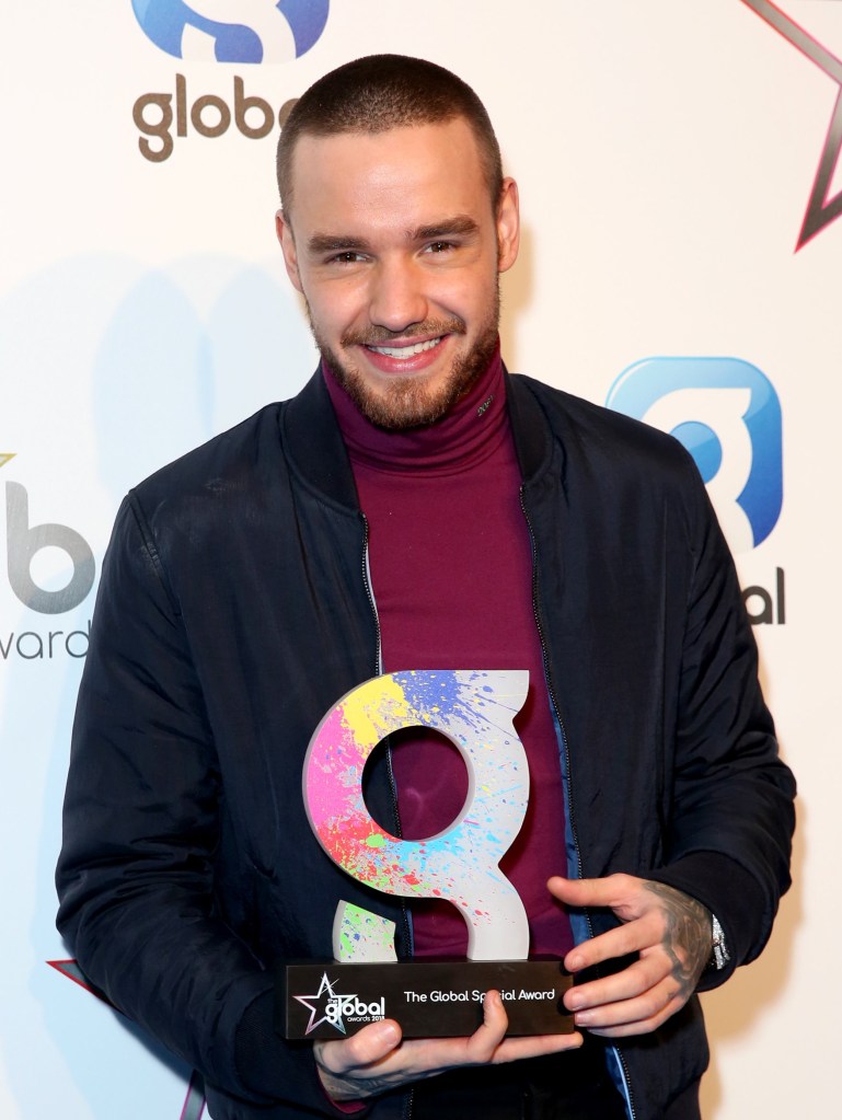 Liam Payne smiling while holding a Global Award. He is wearing a burgundy jumper and a navy blue jacket