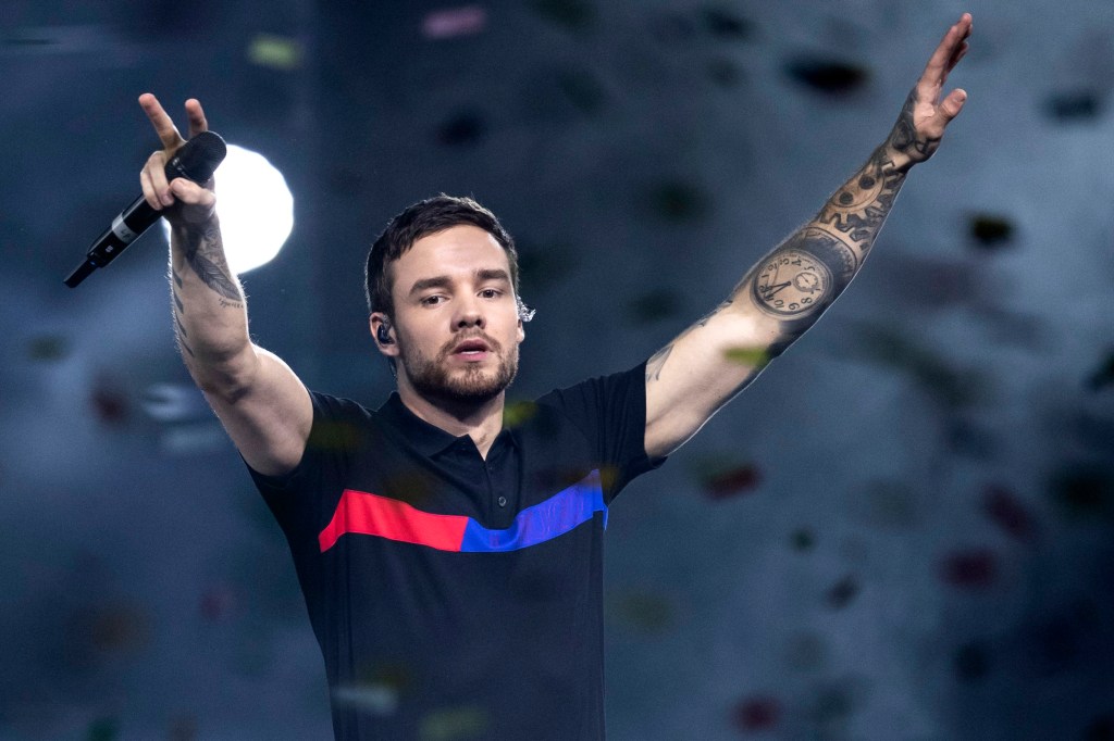 Liam Payne performing on stage, raising both arms in the air