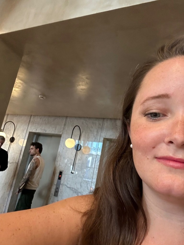 Half selfie of a woman with Liam Payne pictured in the background at a hotel