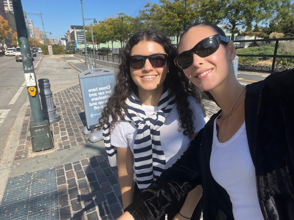 Vittoria Ceretti taking a selfie with a fan. The fan is wearing a white t-shirt with a white and black striped jumper tied loosely around her neck, while Vittoria is wearing a white top and a black jacket