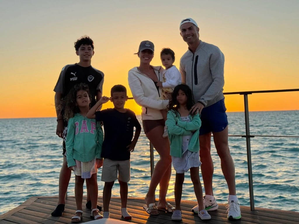 Chrstiano Ronaldo and Georgina Rodriguez posing in front of a sunset and the ocean with their children